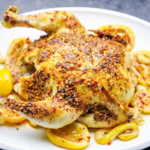 A whole roasted chicken with lemon and nut garnish served on a plate.
