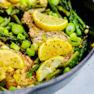 Chicken and asparagus cooked in a skillet with lemon slices, creating a one pot lemon garlic pork chop skillet meal.