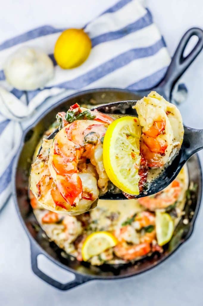 shrimp in a skillet with some on a spoon with lemon and butter