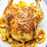A whole roasted chicken with lemons on a plate.