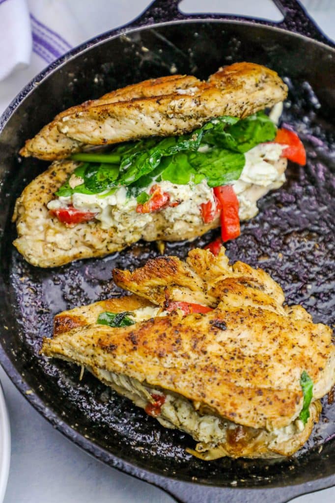 chicken with spinach, cheese, and bell pepper stuffed in the center in a cast iron skillet.