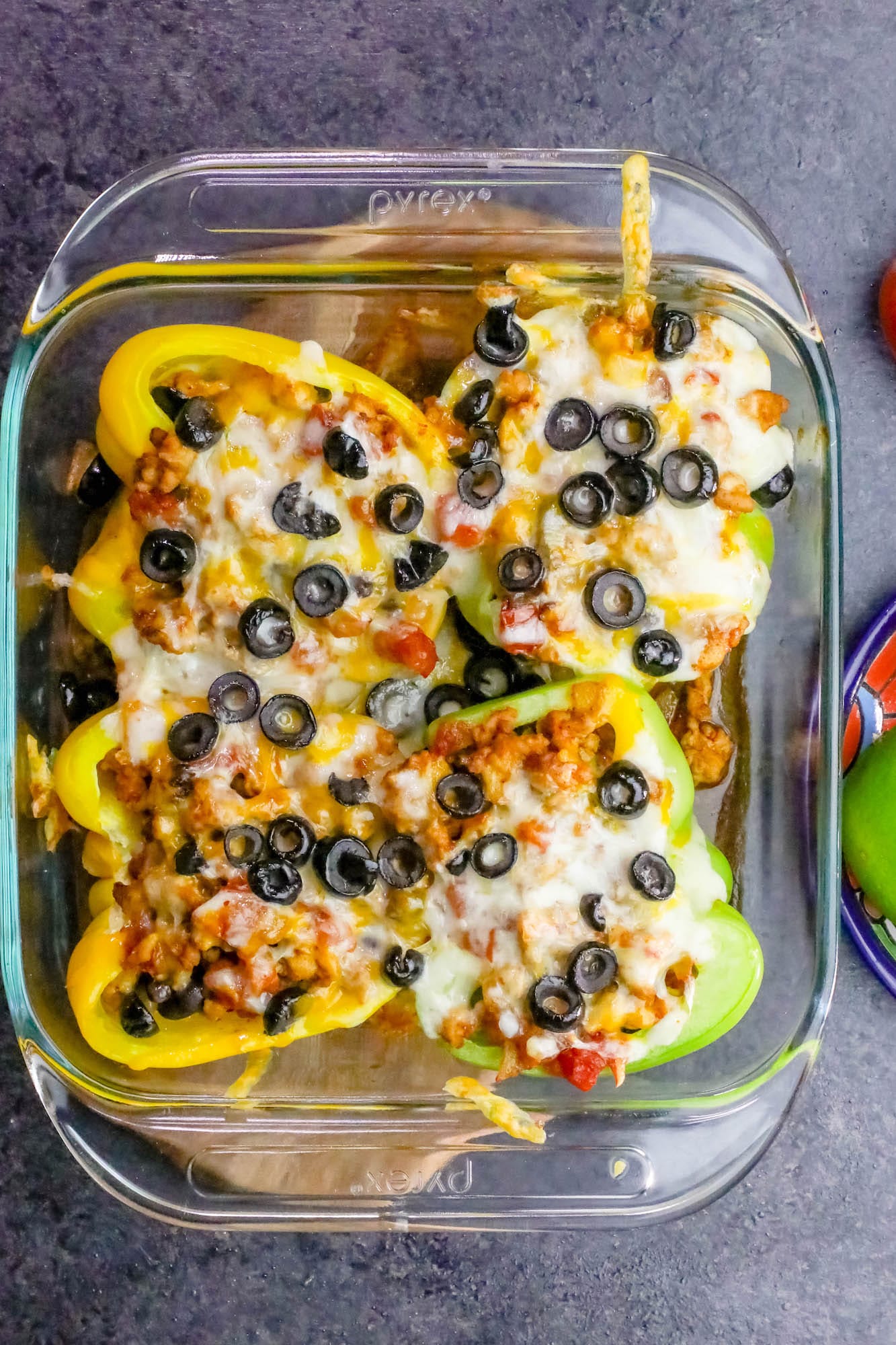 peppers in a casserole dish with cheese and black olives