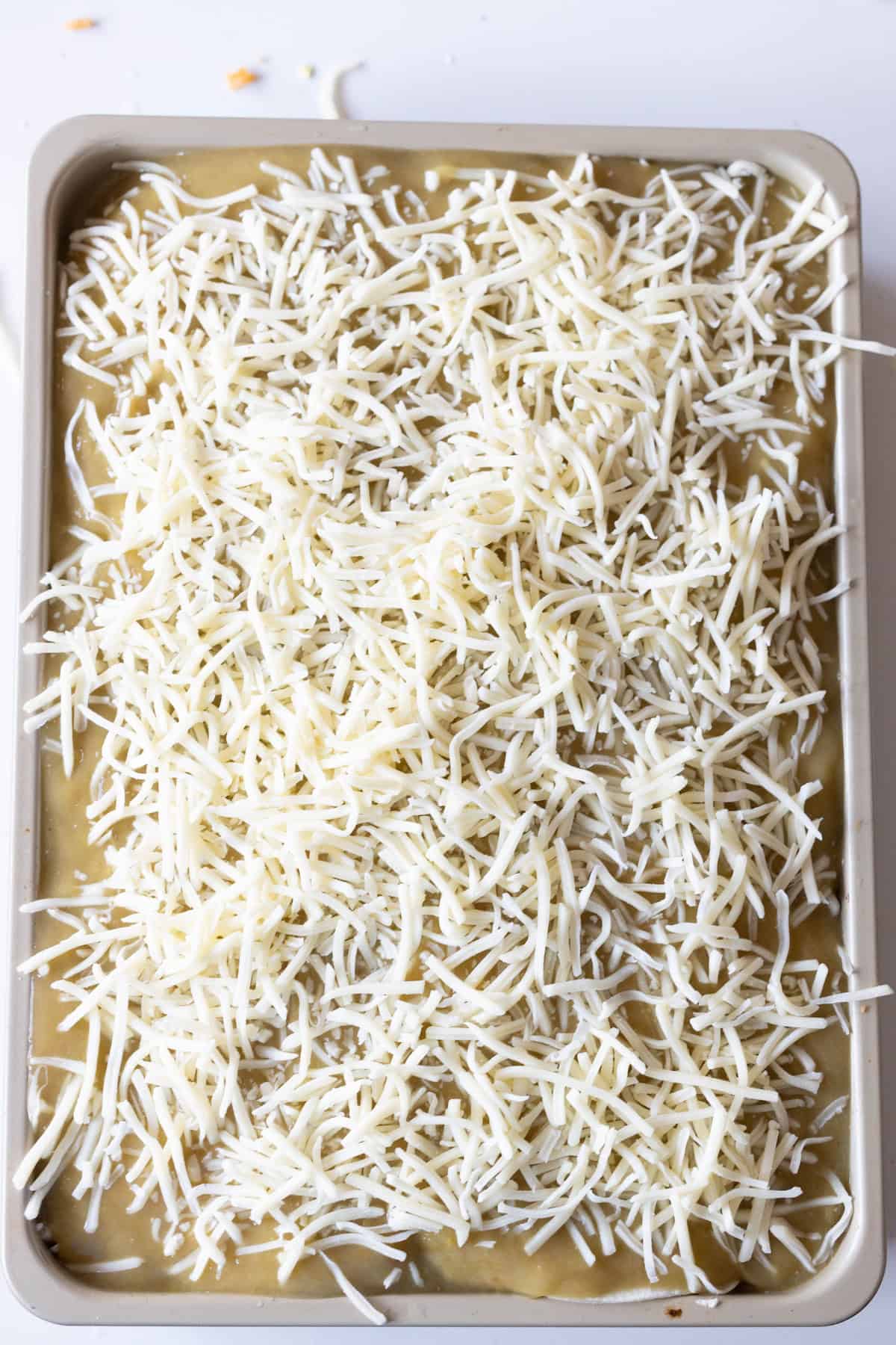 A rectangular baking dish filled with a mixture covered with shredded cheese, ready to be baked into an Easy Chicken Enchilada Pie Bake.