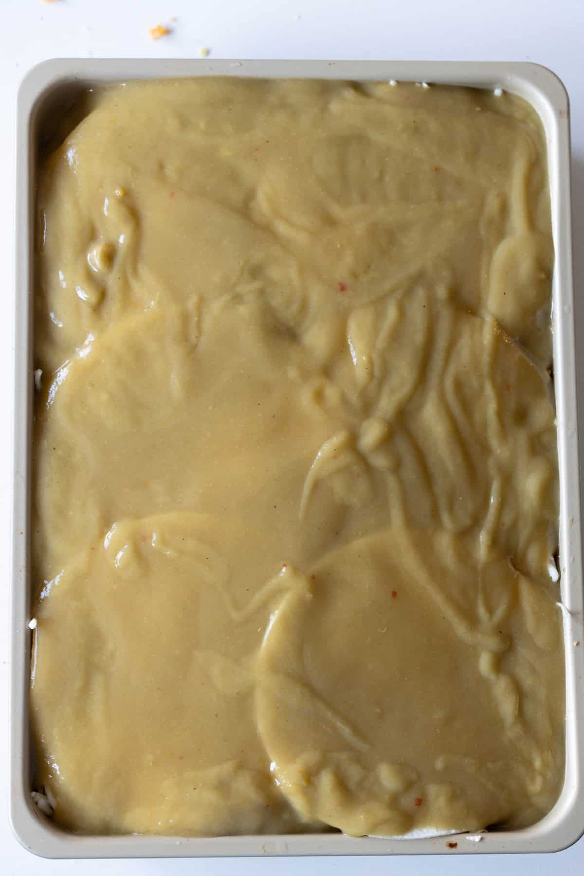 A rectangular baking dish filled with creamy, light brown batter or sauce that appears smooth and slightly thick in texture, perfect for making a delicious Chicken Enchilada casserole.