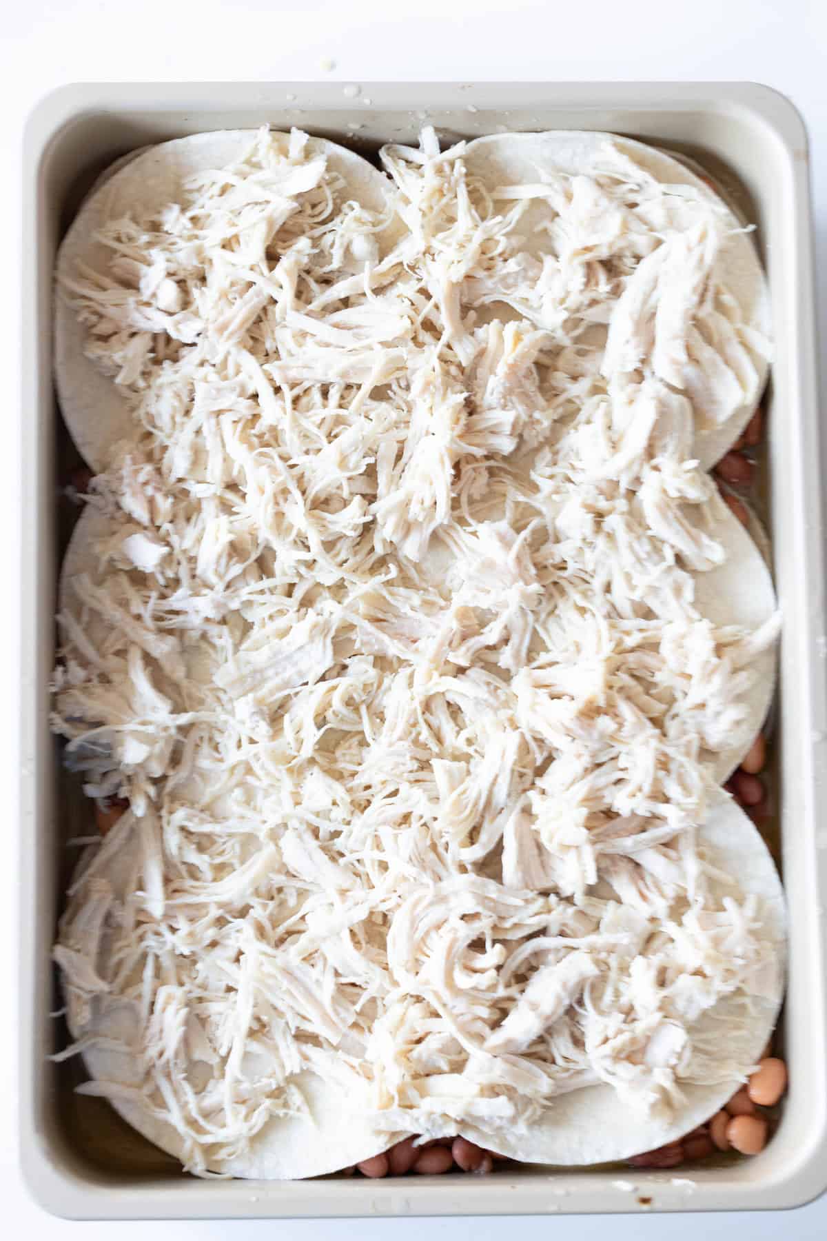 A rectangular baking dish filled with layered tortillas, shredded chicken, and beans creates an Easy Chicken Enchilada Pie Bake.