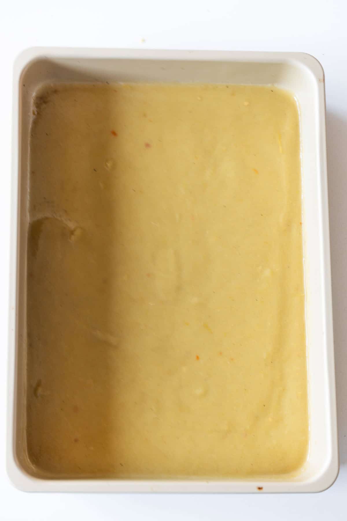 A rectangular baking dish containing smooth beige batter, ready for baking a delightful Easy Chicken Enchilada Pie Bake.