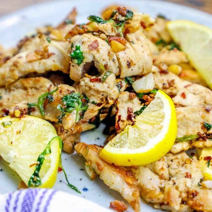 Grilled chicken tenders with lemon slices on a plate.