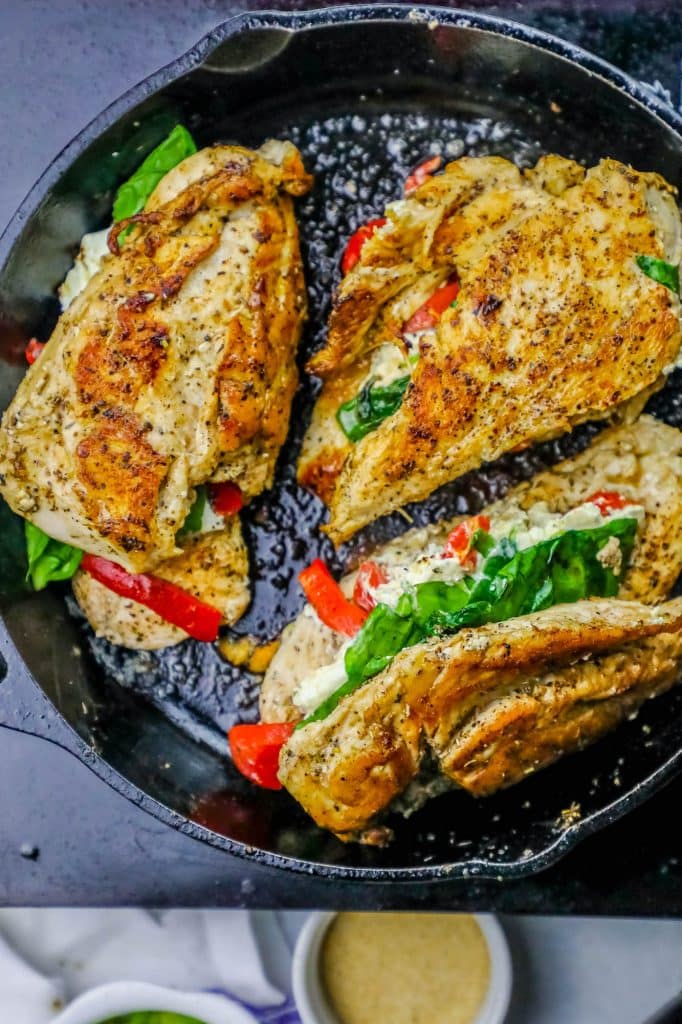 chicken with spinach, cheese, and bell pepper stuffed in the center in a skillet.