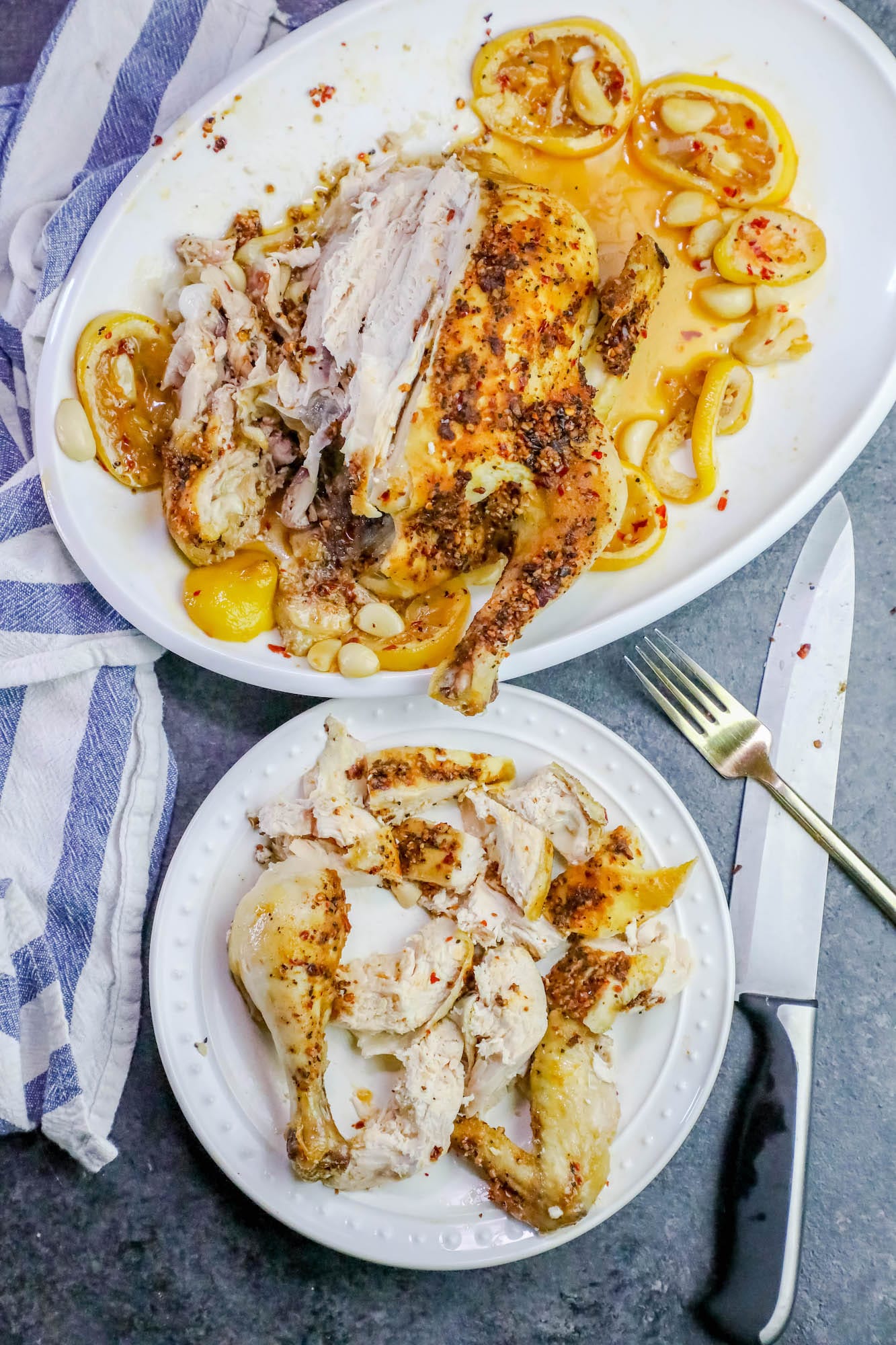 herb covered chicken some on a plate and some still whole on a platter with lemons and garlic