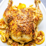 Easy Whole Roasted Montreal Chicken on a white plate with lemons and nuts.