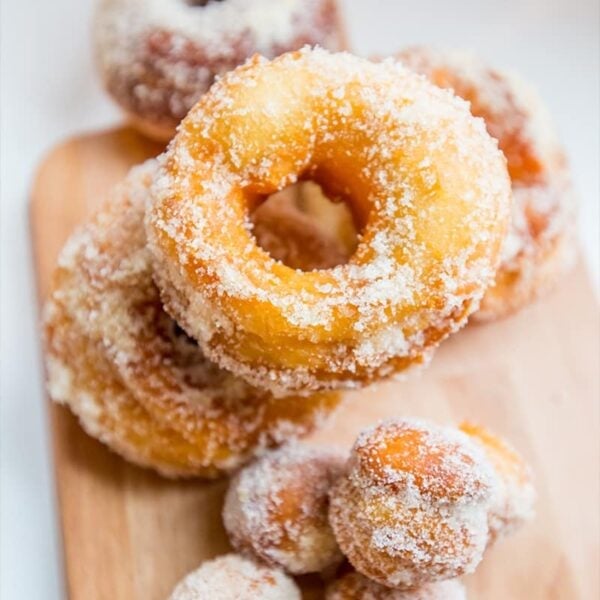A wooden board with sugar-coated 2 Ingredient Easy Mulling Spice Donuts and doughnut holes made from canned biscuits arranged in a pile.