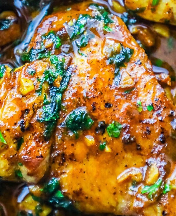 A close up of blackened chicken thighs in a garlic butter sauce.