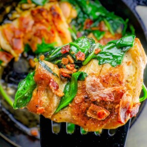 A fork is holding a piece of bacon and spinach in a one pot chicken and spinach dinner.