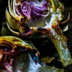 Charred artichokes with a hint of garlic butter, cooked to perfection on a baking sheet.