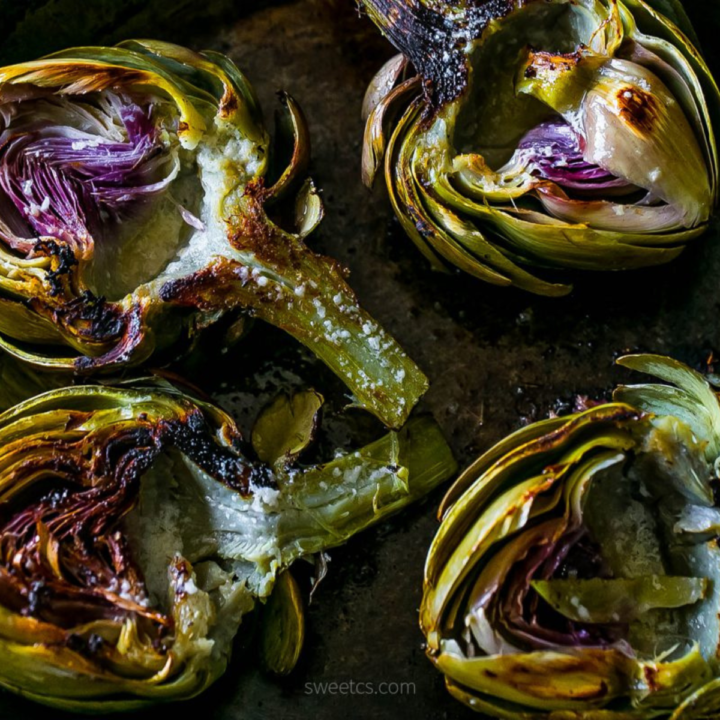 Charred artichokes on a baking sheet with garlic butter.