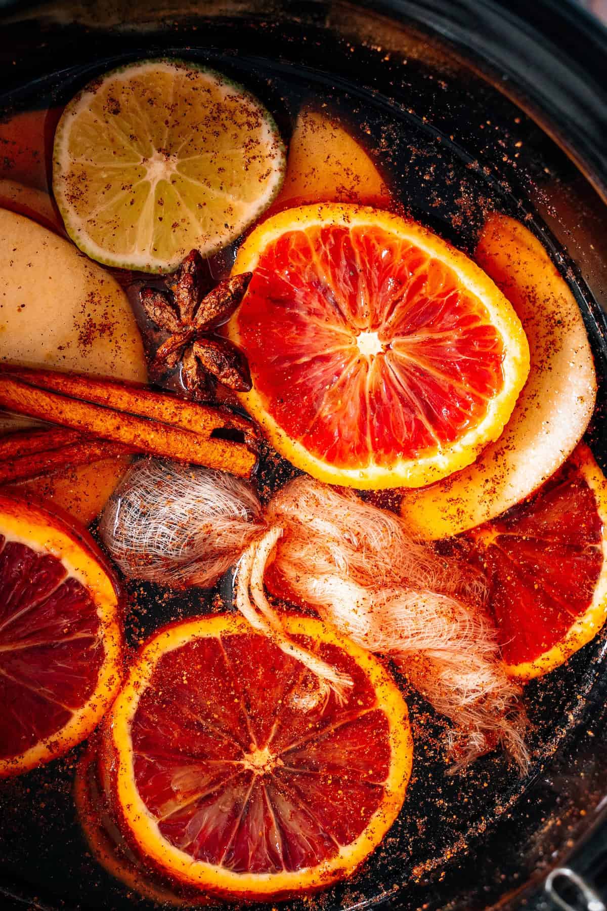 Sliced citrus fruits, apple, cinnamon sticks, star anise, and a spice sachet float in liquid, creating the cozy aroma and flavors of the Best Mulled Cider Ever.