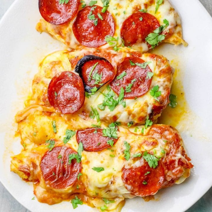 Three keto-friendly pepperoni stuffed chicken breasts on a white plate.