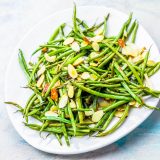 Roasted green beans almondine on a white plate.