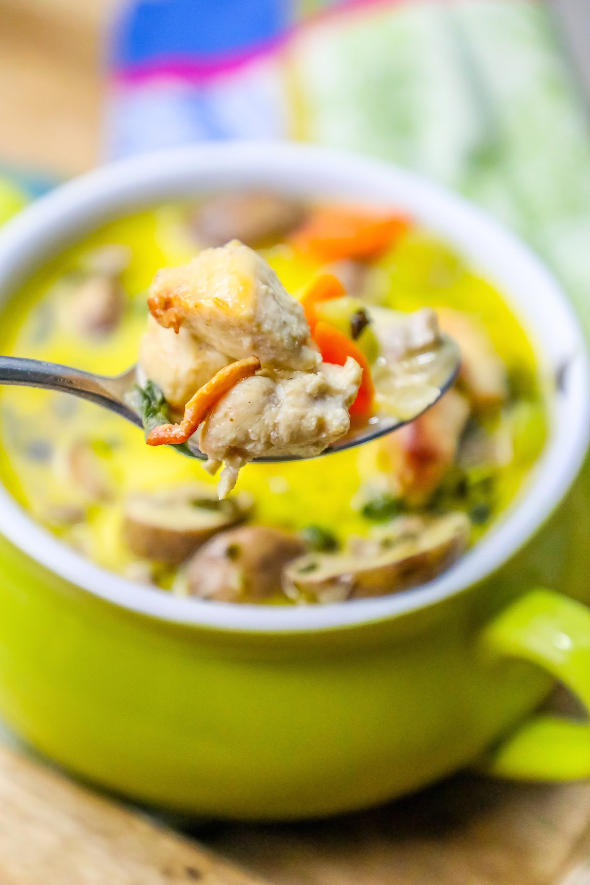 picture of mushroom and chicken soup with thyme on the top in a green pot with a spoonful up close. 