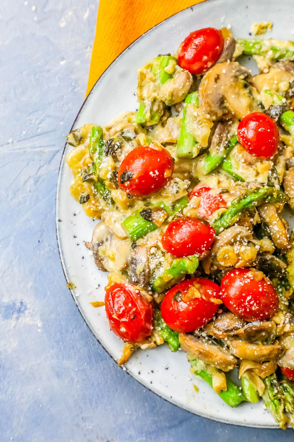 A cheesy and creamy skillet vegetable side dish featuring asparagus, mushrooms, and tomatoes.