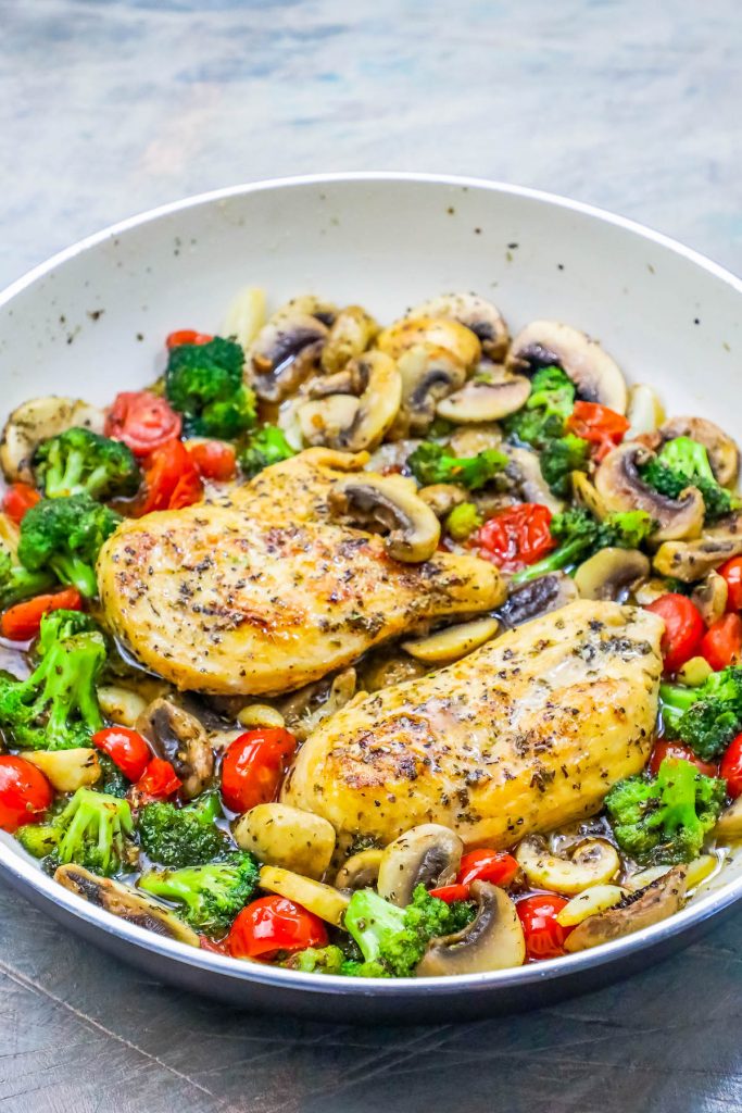 chicken in a bed of broccoli, tomato, and mushrooms and sauce in a pan