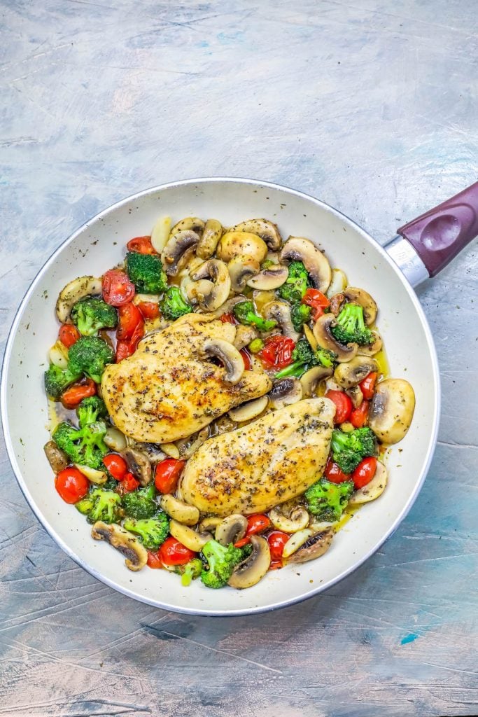 chicken in a bed of broccoli, tomato, and mushrooms and sauce in a skillet