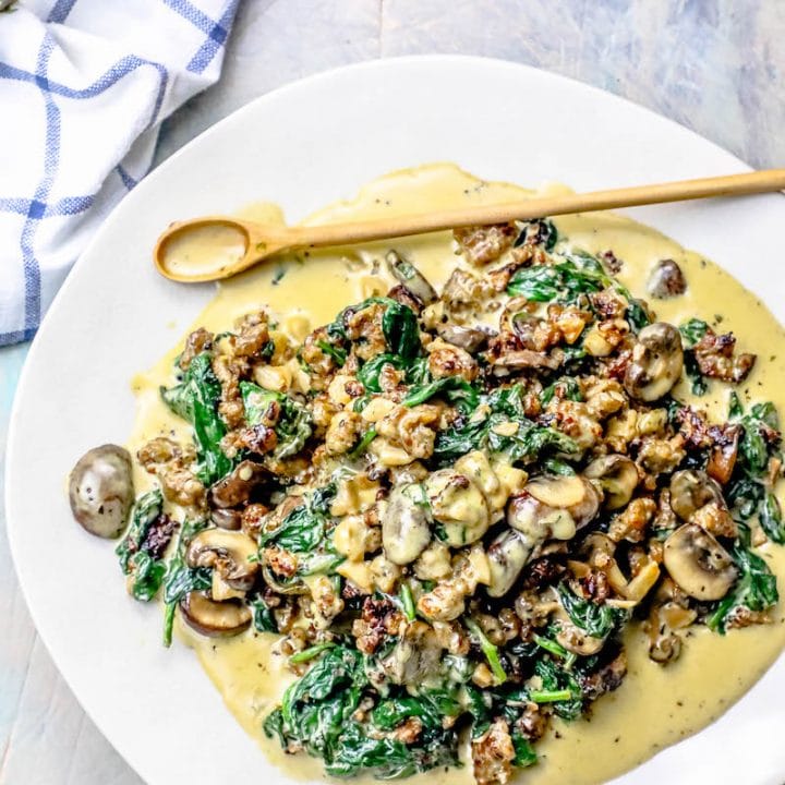A creamy dish of sausage and mushrooms in a spinach cream sauce served on a white plate.