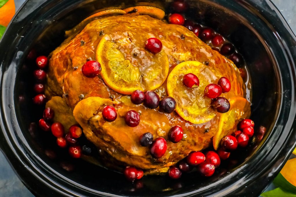 cooked ham in a slow cooker with orange slices and cranberries on it