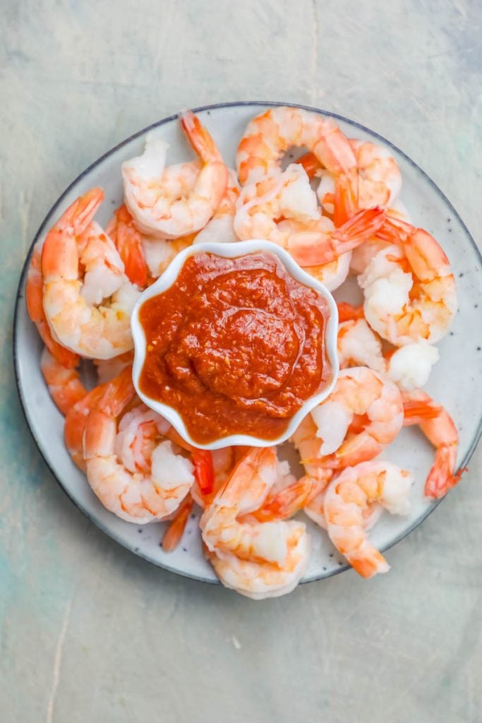 cooked shrimp cocktail on a plate around a cup of bright red cocktail sauce