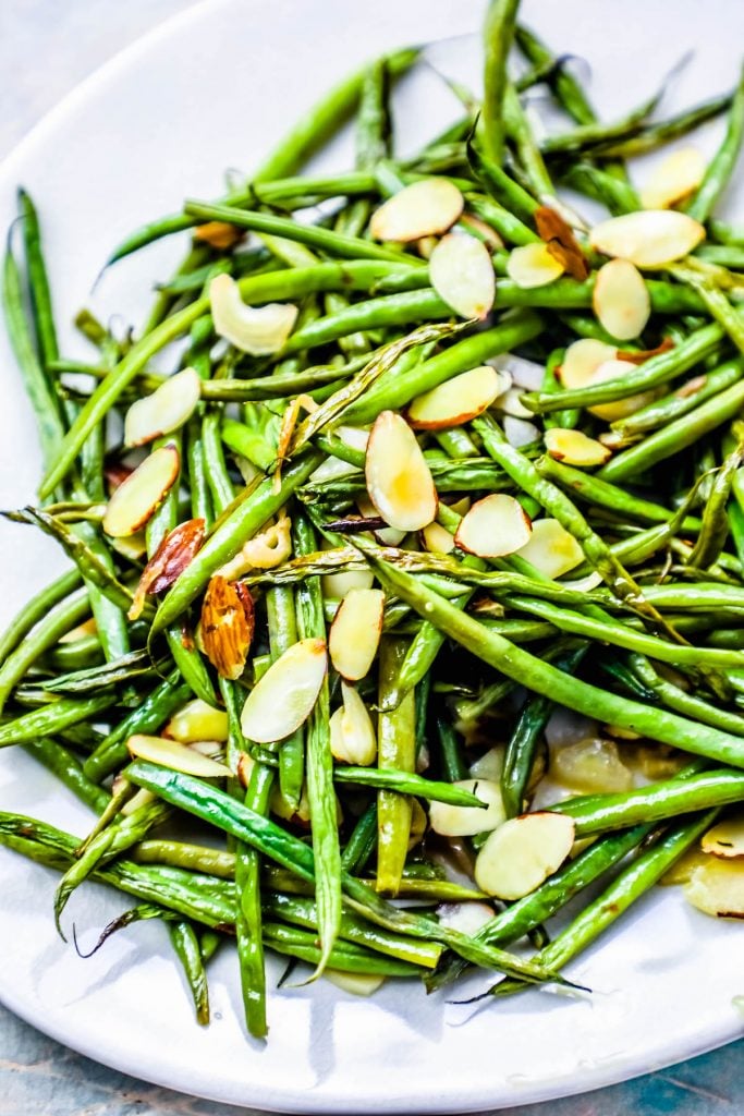 roasted green beans covered in toasted almonds on a white plate. 