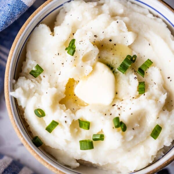 Bowl of Instant Pot Mashed Potatoes topped with a pat of butter, chopped green onions, and black pepper.