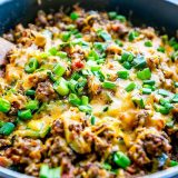 A Cheesy Taco Skillet loaded with beef and vegetables, cooked in a pan with a wooden spoon.