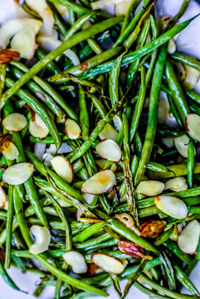 roasted green beans covered in toasted almonds on a white plate. 