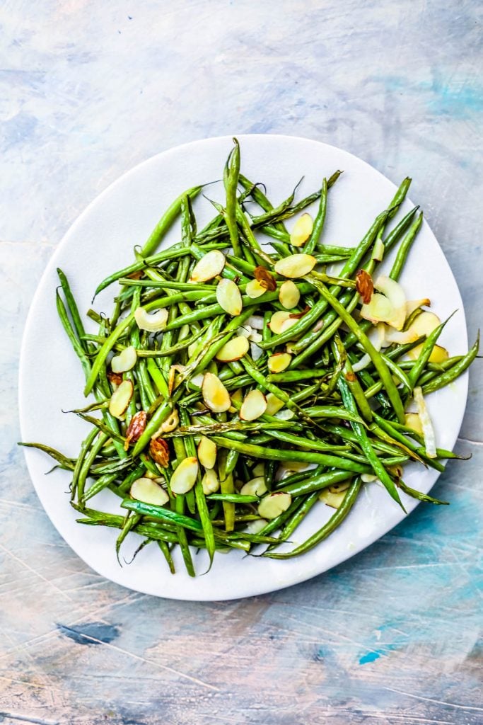 roasted green beans covered in toasted almonds on a white plate. 