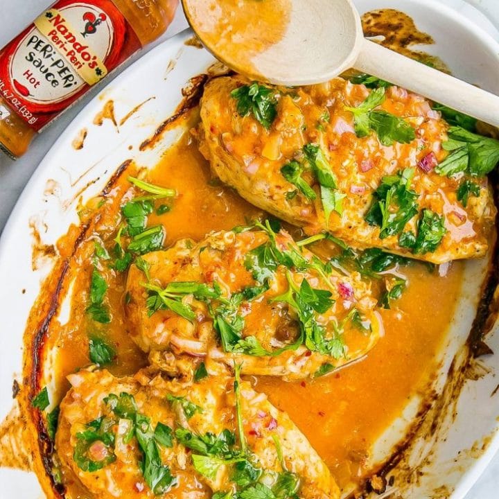 Nandos Peri Peri chicken on a white dish with sauce and a spoon.