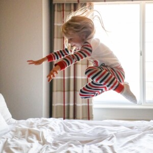 A little girl on a family road trip jumping on a bed in pajamas.