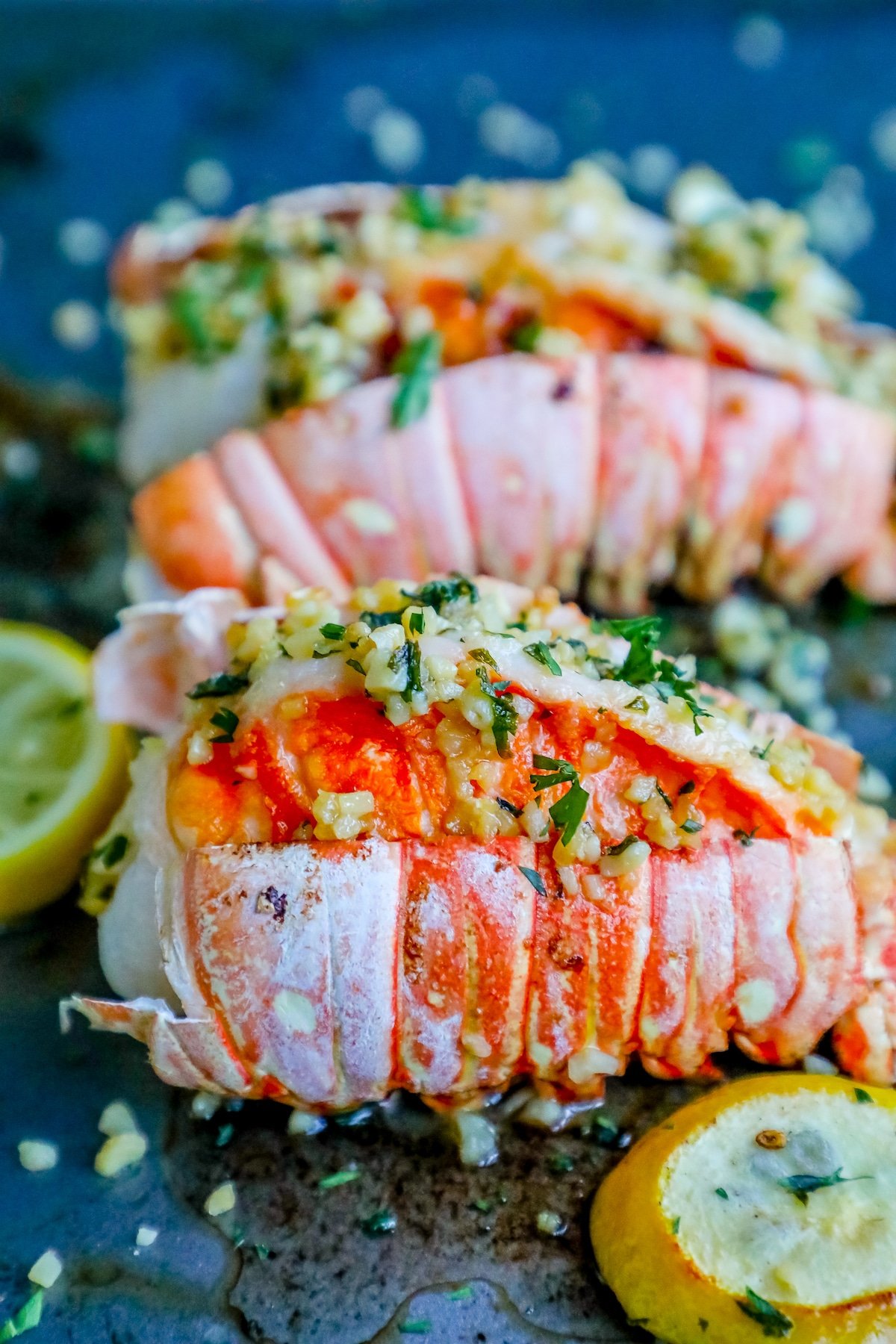 picture of lobster tails on baking sheet with lemon and parsley on top 