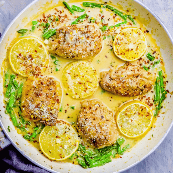 Creamy Lemon Garlic Chicken Thighs and Asparagus in a skillet. This one pot keto dinner is a delicious twist on a classic creamy chicken thigh dish.