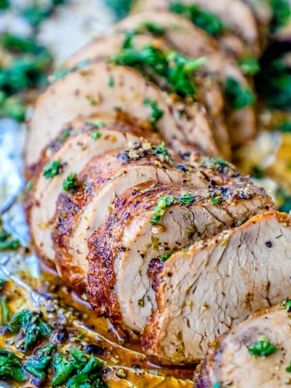 Picture of pork tenderloin sliced and garnished with parsley on tinfoil.