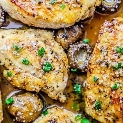 Creamy Garlic Parmesan Chicken breasts in a pan with mushrooms and herbs.