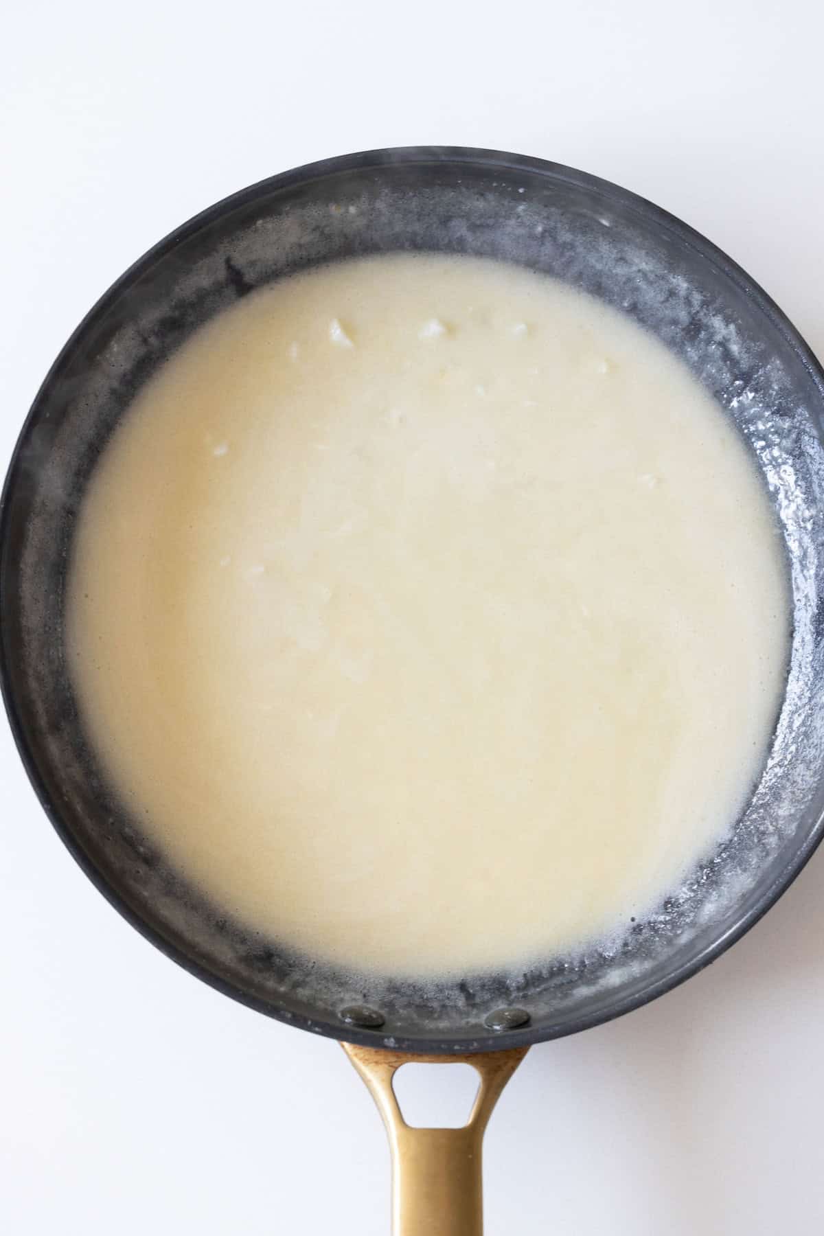 A frying pan on a stovetop contains a thick white sauce, possibly a roux, simmering over low heat—a perfect base for an easy one-pot keto diet dinner.