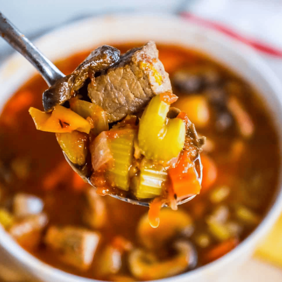 A spoonful of hearty Instant Pot steak soup with chunks of meat and vegetables, above a bowl of the same soup.