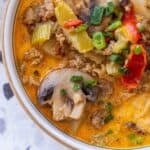 A bowl of soup containing sausage, mushrooms, celery, peppers, and green onions in an orange-colored broth—try this 20 Minute Creamy Sausage and Mushroom Soup for a quick and flavorful meal.