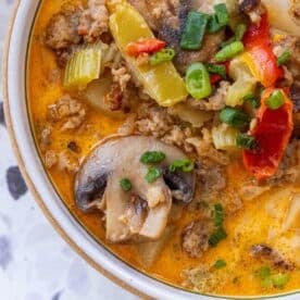 A bowl of soup containing sausage, mushrooms, celery, peppers, and green onions in an orange-colored broth—try this 20 Minute Creamy Sausage and Mushroom Soup for a quick and flavorful meal.
