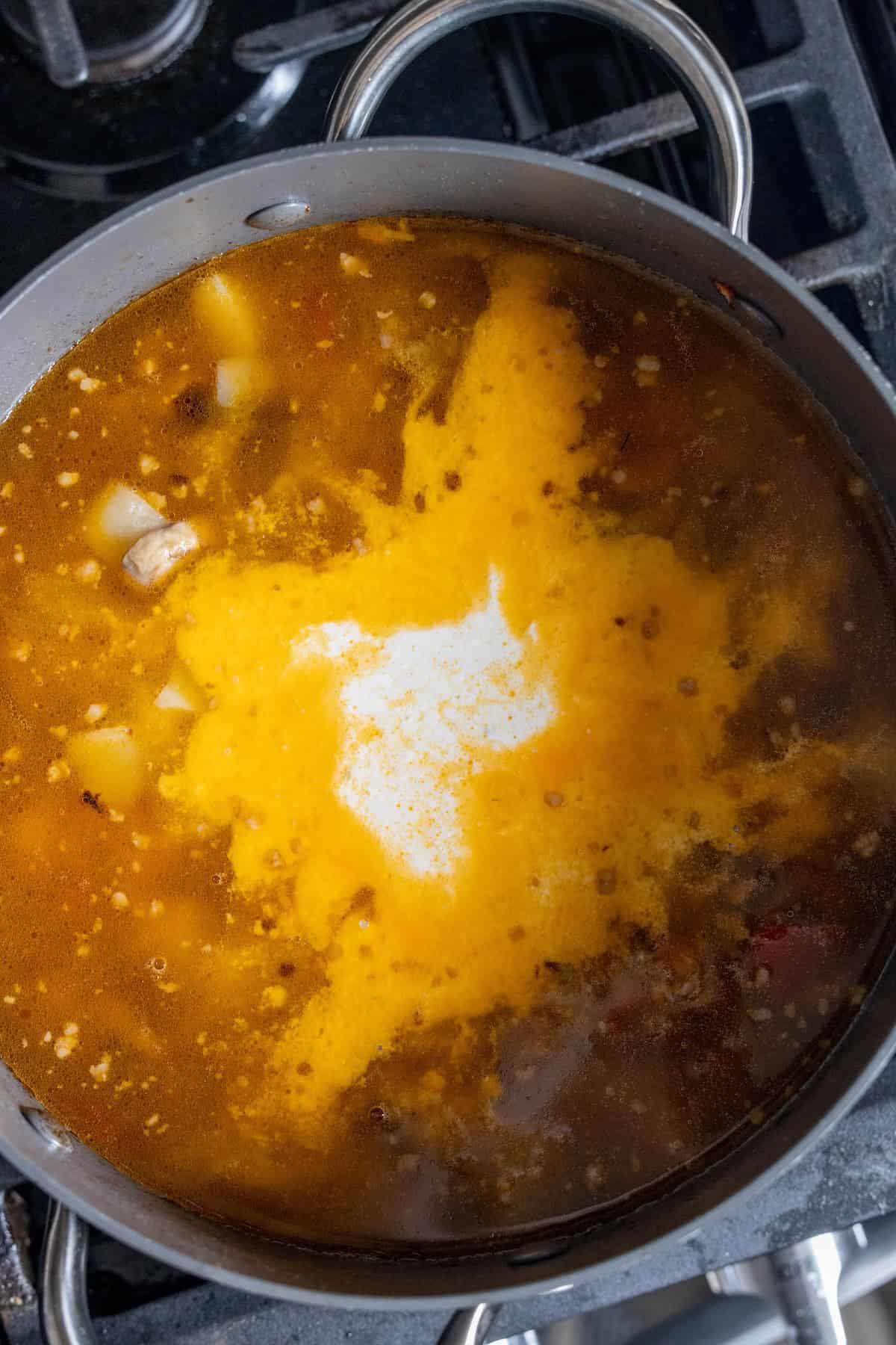 A pot of Easy Creamy Mushroom and Sausage Soup simmers on the stovetop, with diced potatoes and a splash of cream being stirred for a hearty one-pot meal.