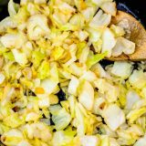 Sauteed cabbage in a skillet with a wooden spoon, an easy keto recipe showcasing pan fried cabbage and onions.