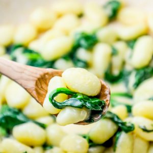 One pot gnocchi recipe cooked with spinach using a wooden spoon.