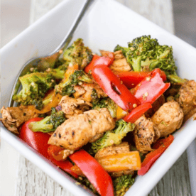 A bowl containing stir-fried Mexican chicken with broccoli and red bell peppers.