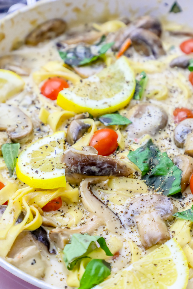 pasta in a pan with mushrooms, tomatoes, basil, a creamy sauce, and lemons