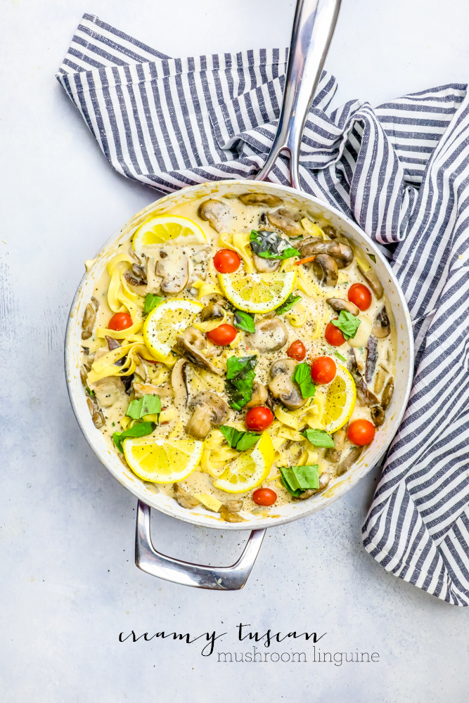 pasta in a pan with mushrooms, tomatoes, basil, a creamy sauce, and lemons